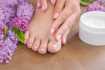 Obraz na płótnie Canvas Young woman's hands applying a foot moisturizing cream. Smooth skin. Spring and summer atmosphere with fresh, fragrant purple lilac flowers.