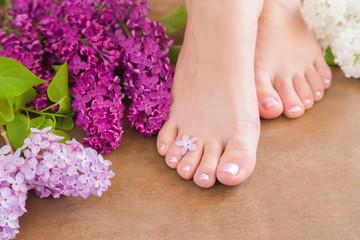 Young woman's feet. Smooth skin. Spring and summer atmosphere with fresh, fragrant lilac flowers.