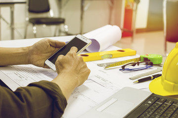 hand  holding mobile phone on the table and notebook pen ruler's helmet, business concept Light sunset background.