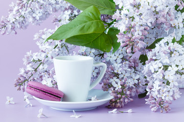 Cup of black coffee, lilac flowers and sweet pastel french macaroon