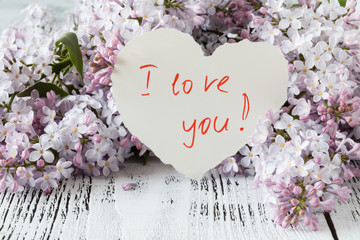 Obraz na płótnie Canvas Lilac flowers on a old wooden background and heart with note i love you