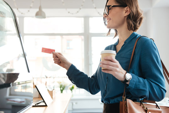 Young lady standing in cafe holding credit card and coffee