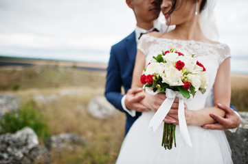 Fantastic wedding couple walking in the tall grass with the pine trees and rocks in the background holding hands.