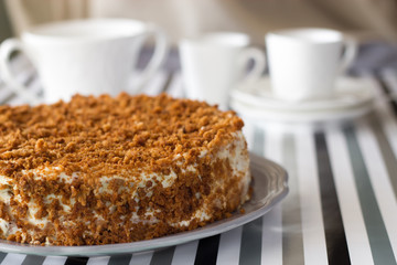 Homemade delicious honey cake with crumb. White tea set on background. Selective focus.