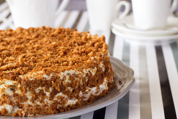Homemade delicious honey cake with crumb. White tea set on background. Selective focus.