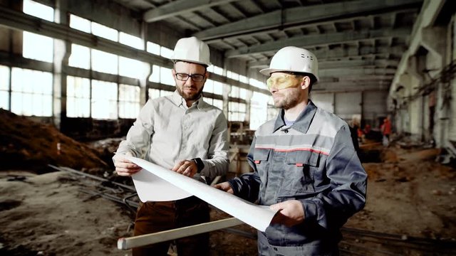 Foreman and chief engineer at the construction site of the factory. The engineer checks the drawing and discusses further plans with the employee.