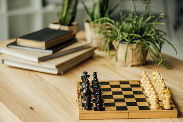 Chess board set for a new game on the table with books and potted plants