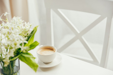 close up of cup of coffee with bouquet of flowers on white tabletop