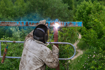 Welder at work. Welder cooks metal grate on the ground blowtorch on the ground in special clothes and mask welder.