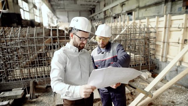 Architect and chief foreman at the construction site of the plant. Men discuss drawbacks in the drawing. Against the background of construction work.