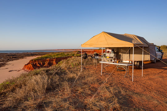A couple enjoying a wine and sunset with off road camper trailer set up at James Price Point, Kimberly, Western Australia