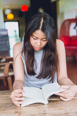 Enjoy relax times with reading book, Asian women Thai teen serious focus to read pocket book in coffee shop.