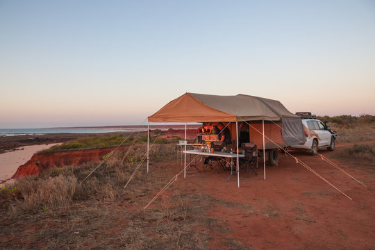 Man preparing a meal under awning of Off road camper trailer at sunset at James Price Point, Kimberley Australia