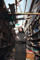 Fototapeta na wymiar Young woman in coat standing in a book warehouse