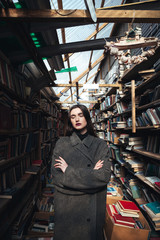Obraz na płótnie Canvas Young woman in coat standing in a book warehouse