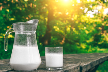 Jug and glass of cold milk on the wooden table. Fresh dairy products. Nature background.