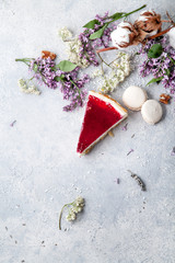 Berry cheesecake slice on light gray concrete background with lilac flowers. Rustic concept with copy space