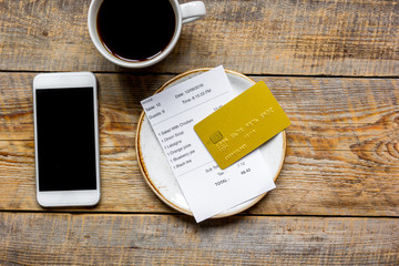 credit card for paying, mobile and check on cafe wooden desk background top view mock up