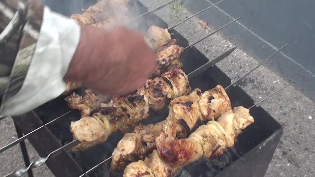 Smoking chicken on grill nearly ready, a hand sprinking water and then taking a spitter 