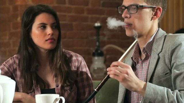 Beautiful couple smokes hookah and talk in the bar