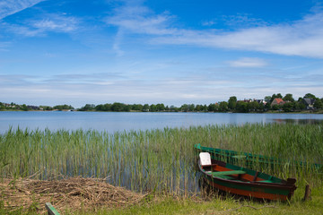 Obraz premium Green boat in the lake on sunny summer day in Lithuania, Trakai. Concept of tranquil country life. Excellent for flyer, post card, advertising, blog, instagram, calendar, notebook, wallpaper