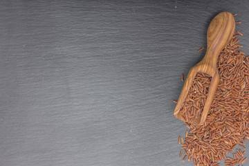 Red rice and olive wood scoop on black background of slate or stone. 