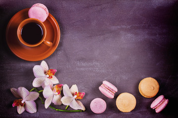 Coffee, orchids and cake macaron or macaroon on gray background from above. Flower, drink and coockie still life. Flat lay, top view. Soft pink toning