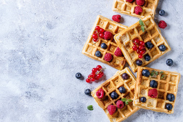 Homemade square belgian waffles with fresh ripe berries blueberry, raspberry, red currant over gray texture background. Top view with space - 159575781