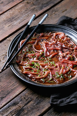 Asian style Beef carpaccio with soy sauce, chive onion, black sesame, served on vintage metal tray with textile napkin and chopsticks over old wooden plank background. Close up