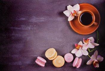 Coffee, orchids and cake macaron or macaroon on gray background from above. Flower, drink and coockie still life. Flat lay, top view. Soft pink toning