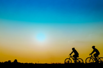 Fototapeta na wymiar Silhouette of cyclists riding bikes on road at sunset.