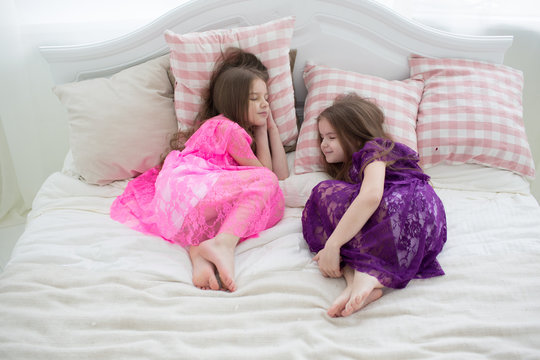 Pretty girls in pink and purple dresses sleep in bed