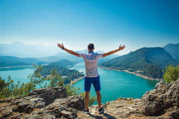 man on a mountain with a beautiful view of the lake and spread his arms out