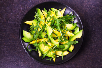 Avocado, mango and arugula salad on black plate. View from above, top studio shot