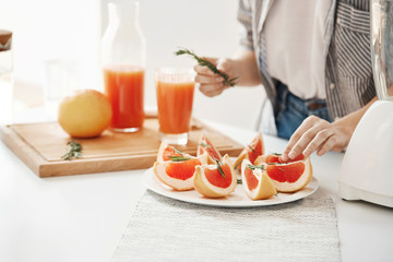 Close up of girl decorating plate with sliced grapefruit and rosemary. Fitness nutrition concept. Copy space.