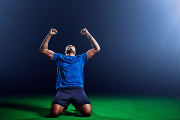 Male soccer player kneeling with arms raised