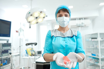 Shot of s female doctor wearing surgical mask and sterile medical gloves holding pink ribbon breast cancer awareness symbol posing in an operating theatre healthcare medicine mammalogy concept.