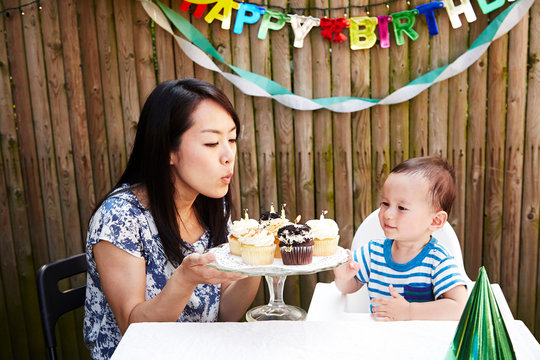 Mother blowing out candles on baby boy's birthday cakes