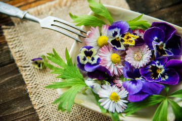 Fresh salad with smoked salmon, black olives, cherry tomatoes and edible flowers on wooden background.