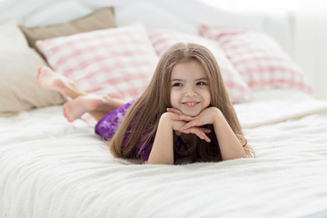 Obraz na płótnie Canvas Sweet girl in purple dress in bed with cushins