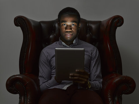 Portrait of sinister young man in armchair with digital tablet