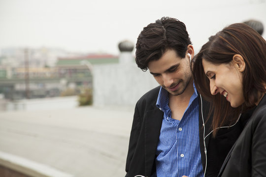 Couple listening to shared earplugs on city roof