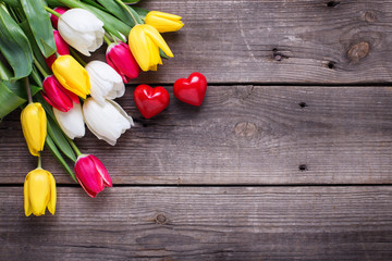Little decorative hearts and bright  spring  tulips flowers on wooden background.  Selective focus. Flat lay. Place for text..