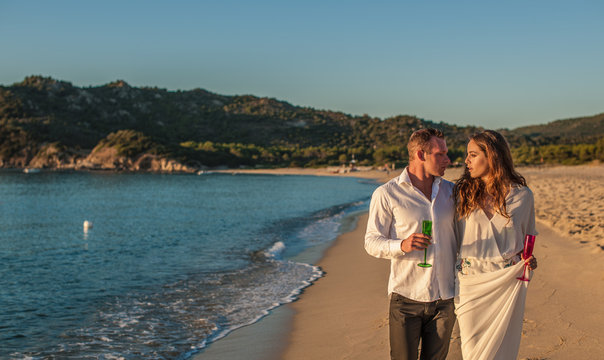 Young couple strolling with champagne on beach, Castiadas, Sardinia, Italy