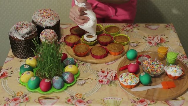 The girl decorates Easter cupcakes with vanilla