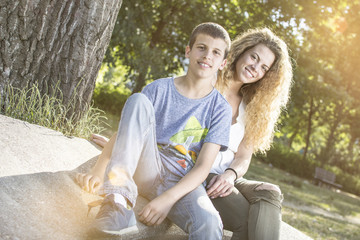 Brother and sister bonding at the park. Smiling and looking at the camera. Lens flare in the background.