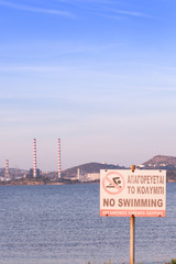 Fototapeta na wymiar No Swimming sign by the beach, with power plant station in the background. Lavrio, Greece.