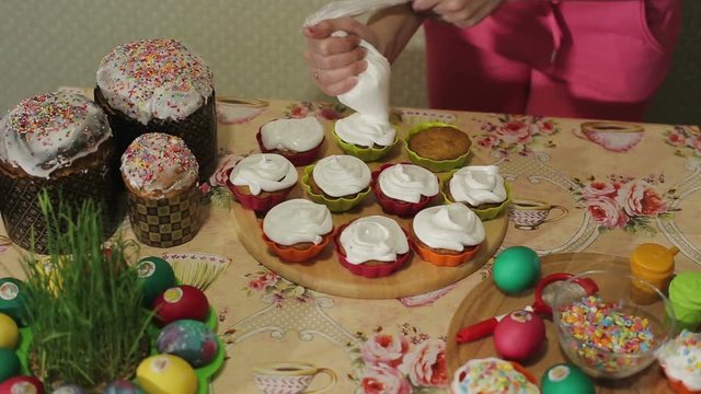 The girl decorates Easter cupcakes with vanilla