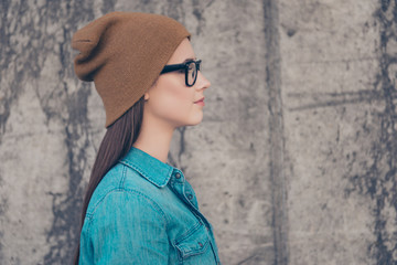 Close up profile side portrait of young stylish lady in casual outfit, hat and glasses near concrete wall outdoors with copy space