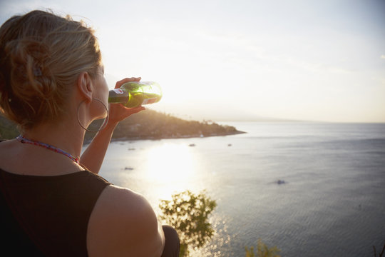 Woman drinking bottle of beer looking out to sea, Amed, Jemeluk beach, Bali, Indonesia